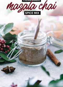 a glass jar of chai spices with a small wooden spoon on a white table with the words "homemade masala chai spice blend" in black and white writing