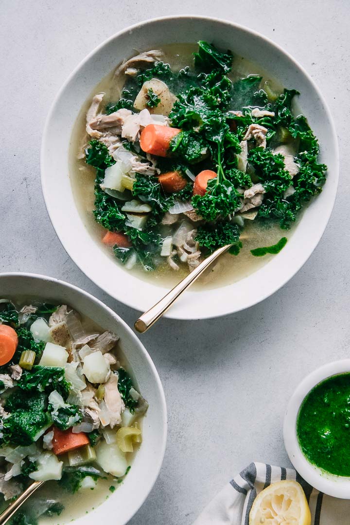 two bowls of chicken kale soup on a white table