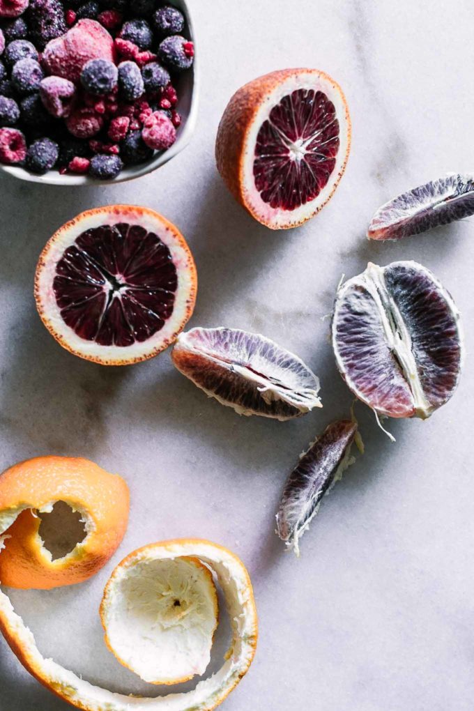 peeled blood oranges on a white table with a bowl of berries