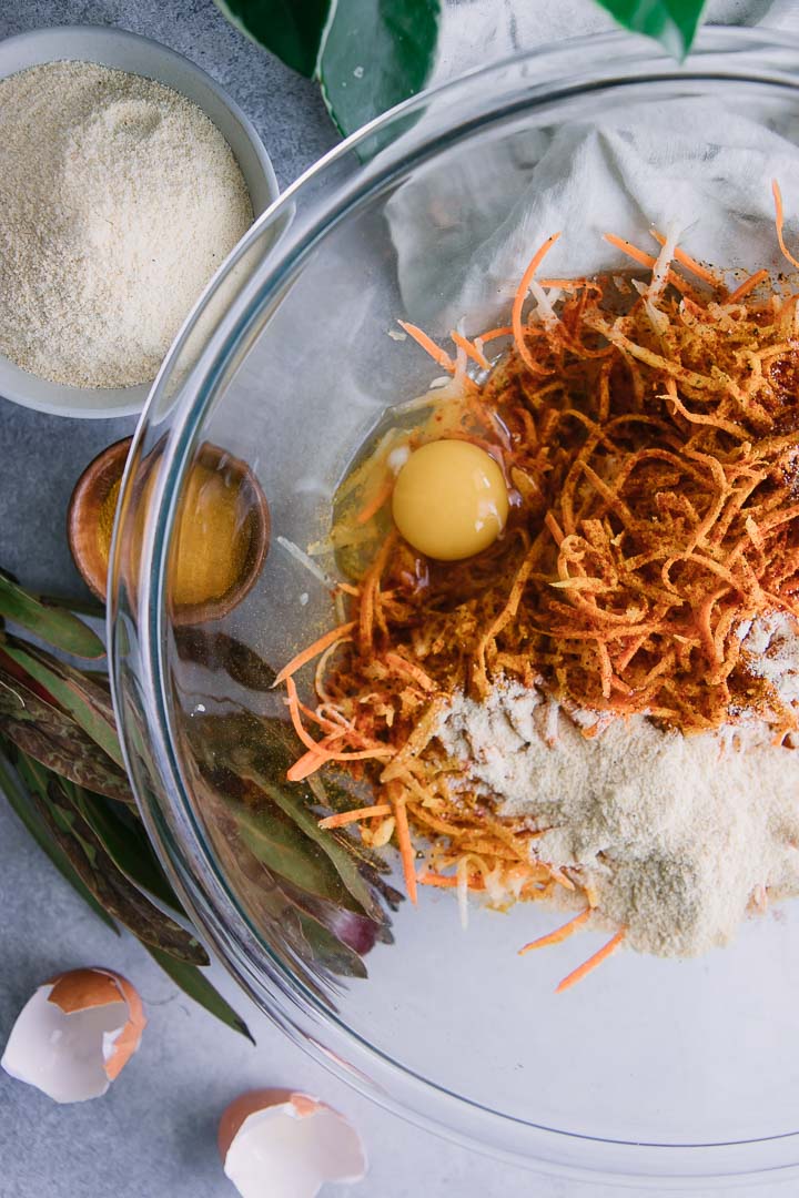 a glass mixing bowl with shredded turnips, carrot, and an egg