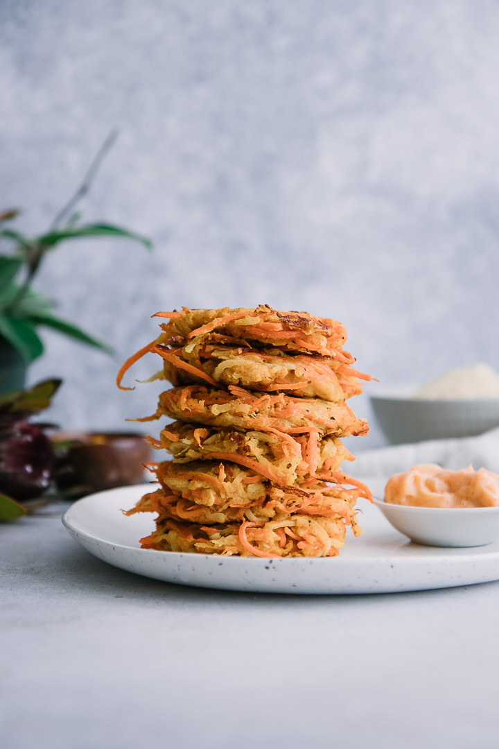 stacked vegetable cakes made of turnips and carrots on a white plate on a table with a plant in the background