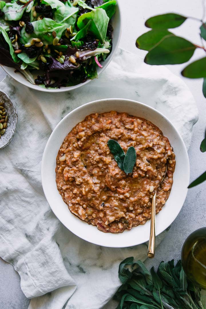 a bowl of zuppa di farro soup on a white table with a sage leave as garnish and a gold spoon and white napkin