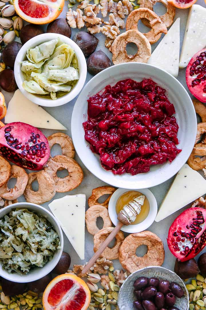 a platter with cranberry sauce, cheese, artichokes, sauerkraut, olives, and nuts