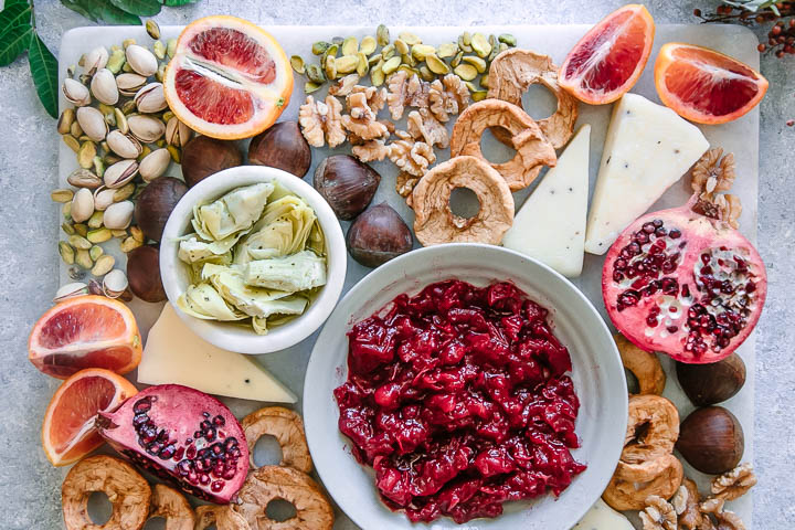 a marble platter with cheese, pomegranates, nuts, and fruit