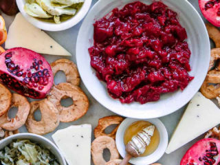 a platter with dips, pickled vegetables, dried, fruit, and honey with the words "how to build a winter harvest cheese board" in black writing