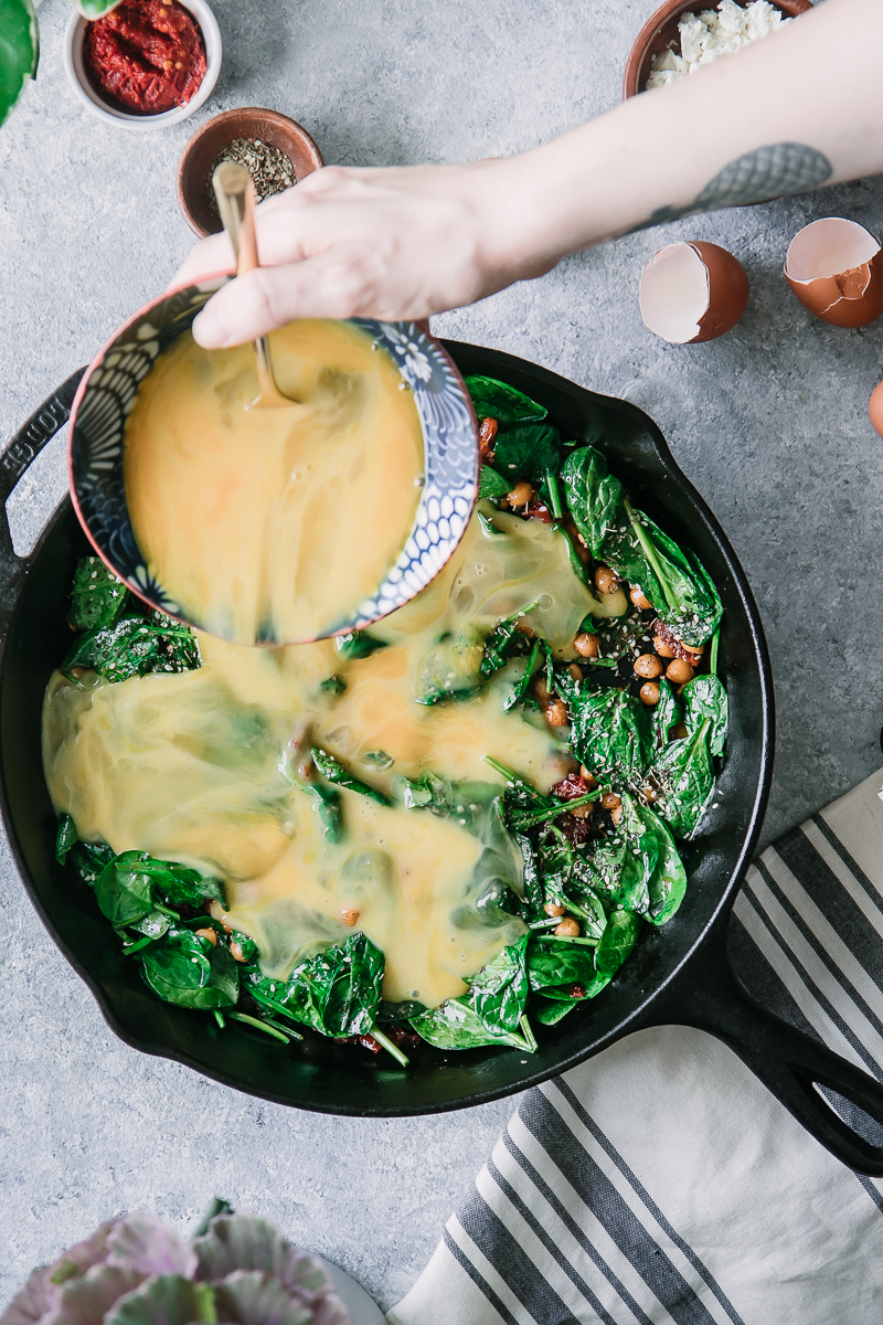 a hand pouring whisked eggs into a cast iron skillet to make a frittata