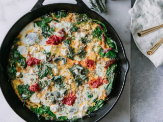 a spinach frittata in a cast iron skillet with feta cheese and red harissa and the words "mediterranean chickpea harissa frittata" in black writing