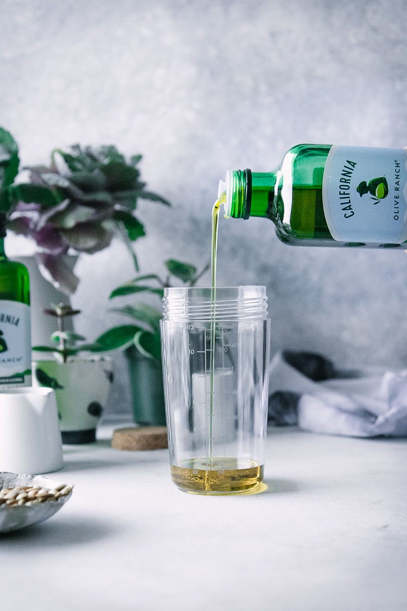 Oil drizzling into a salad shaker on a blue table