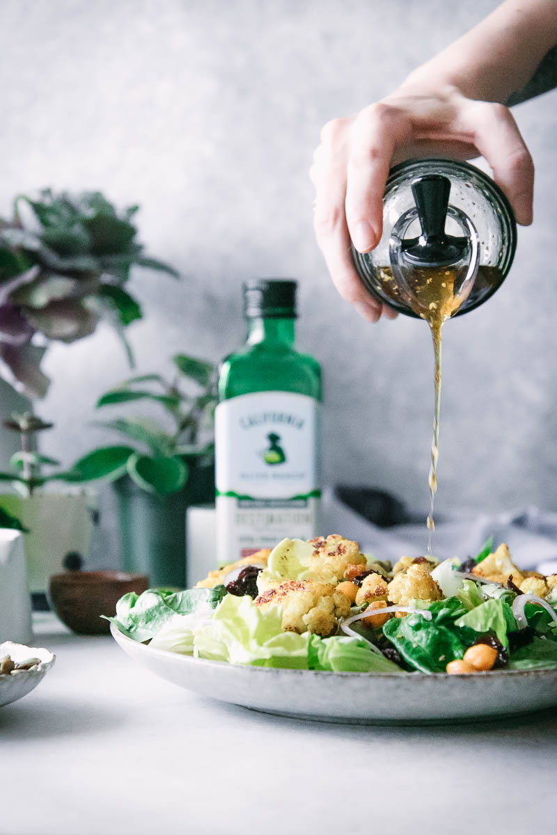a hand drizzling salad dressing onto a salad on a white table
