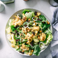 a simple greens salad with cauliflower and chickpeas on a white plate on a table with a blue napkin