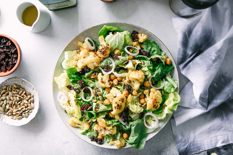 a simple greens salad with cauliflower and chickpeas on a white plate on a table with a blue napkin