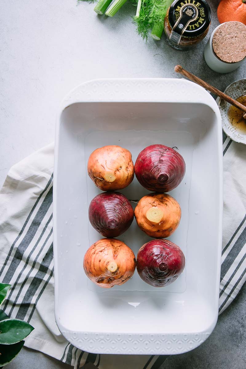 red and golden beets in a white baking dish on a white table 