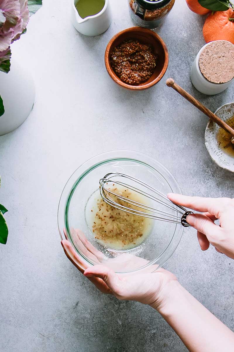 a hand whisking homemade salad dressing in a glass mixing bowl on a white table