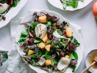 Beet and fennel salad on a white plate and a white table with the words "Roasted Fennel Beet Salad with Homemade Honey Mustard Vinaigrette" in black writing