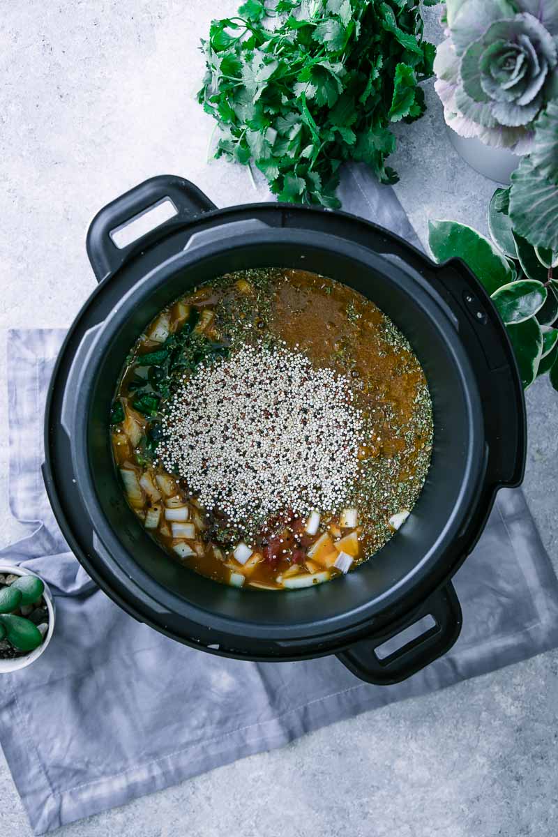 an instant pot pressure cooker filled with vegetable broth, vegetables, and quinoa