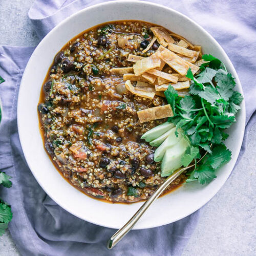 a white bowl of chili made with black beans with avocado, cilantro, and tortillas strips