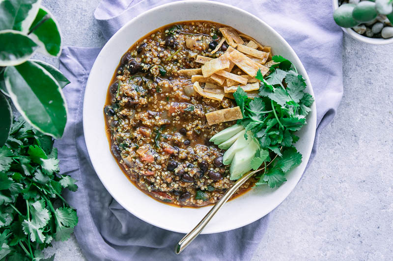 a white bowl of chili made with black beans with avocado, cilantro, and tortillas strips