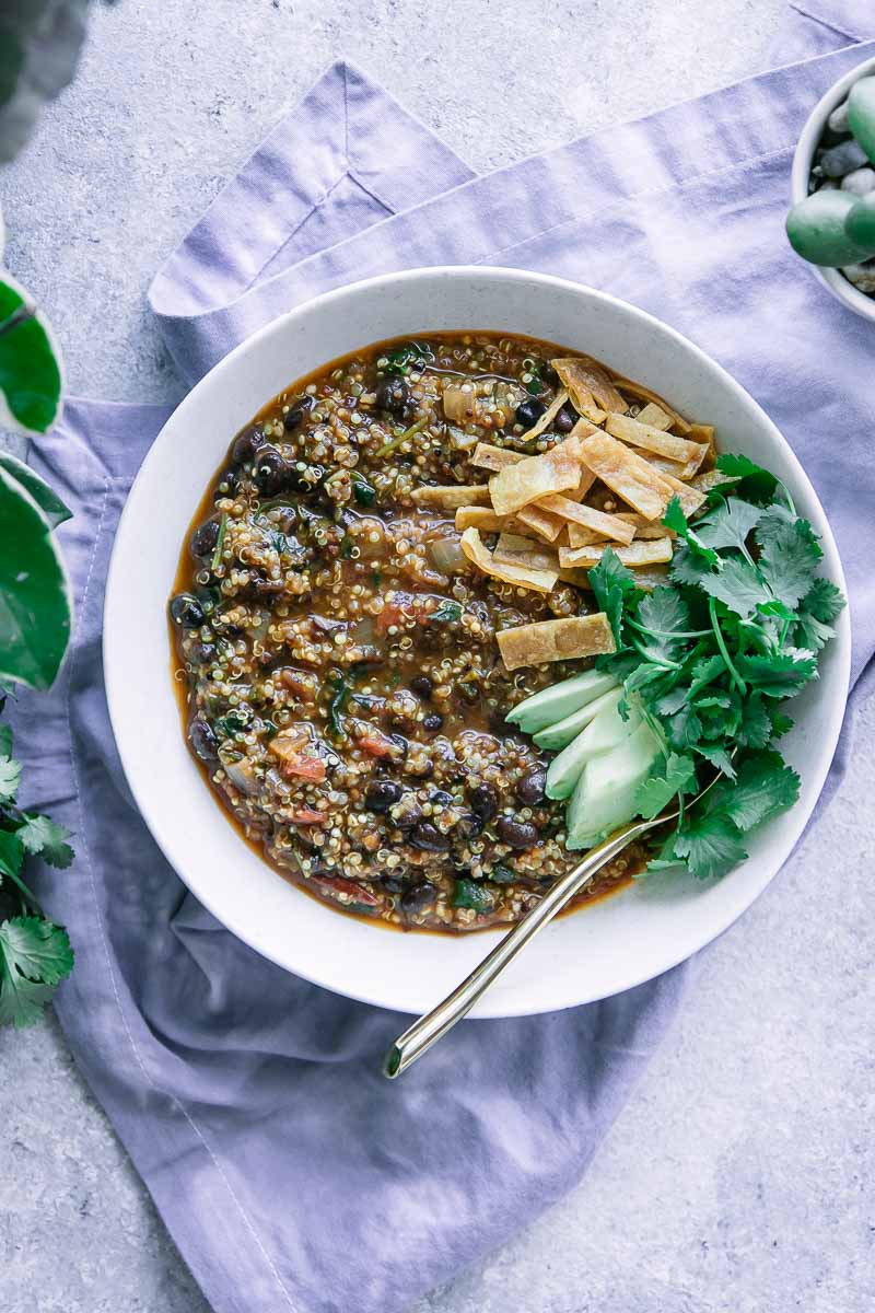 a bowl of black bean quinoa chili on a blue napkin on a white table with a green plant