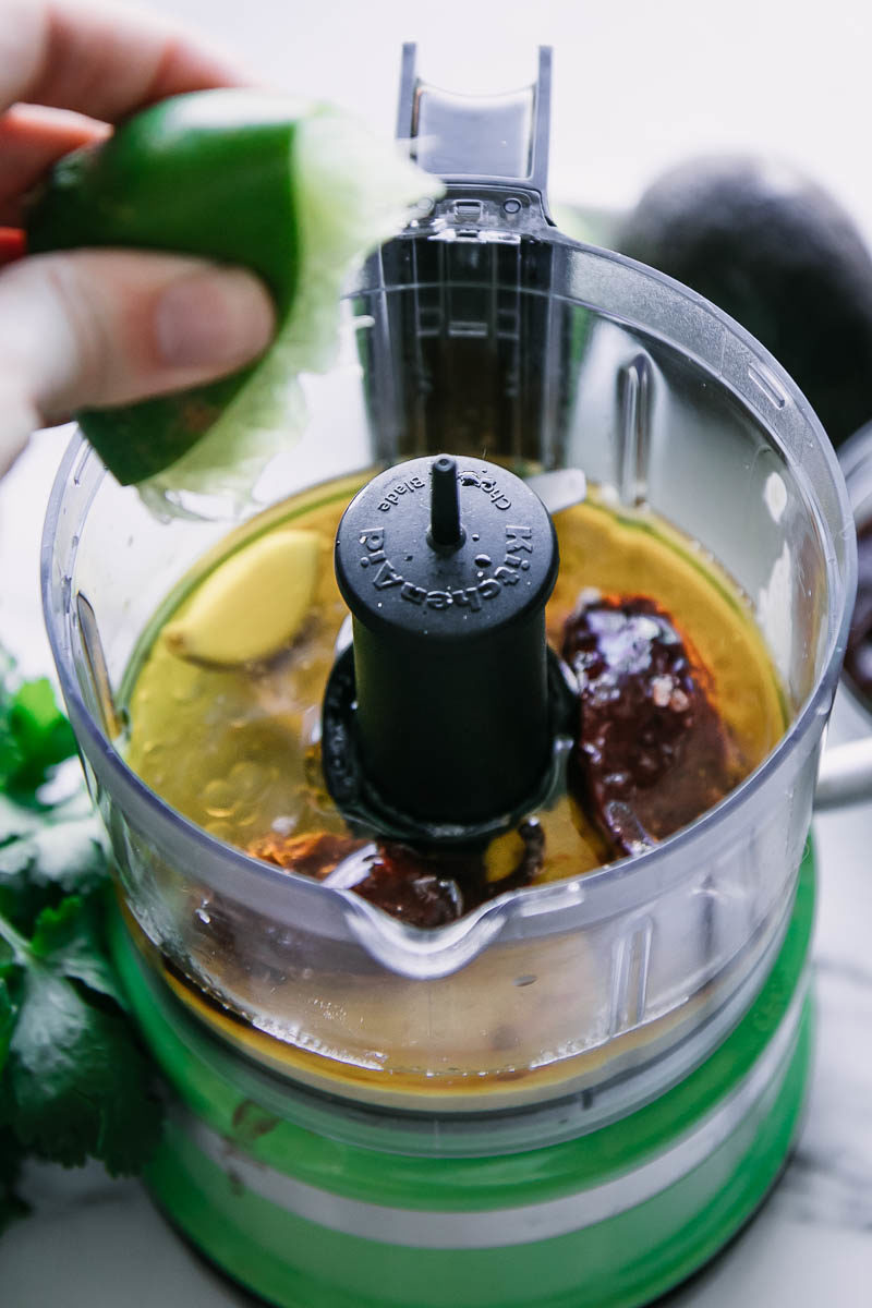 a hand squeezing juice from a lime into a food processor