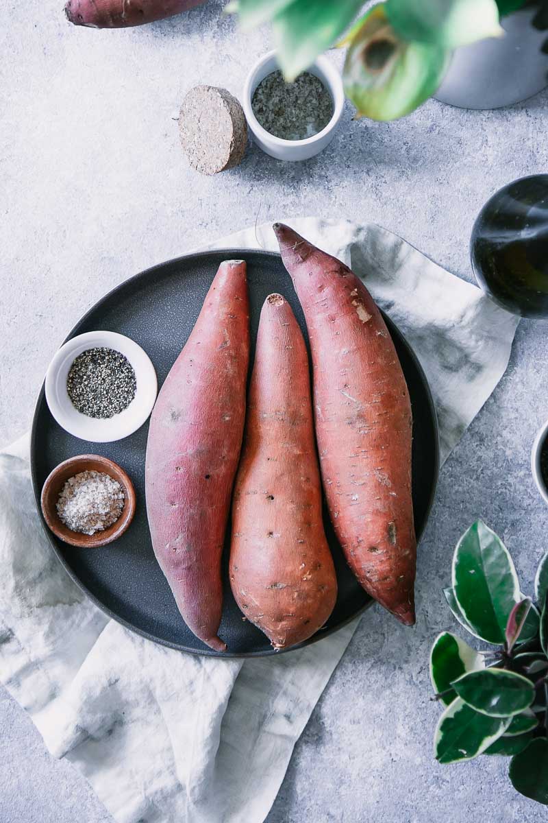 three sweet potatoes on a blue plate with bowls of salt and pepper