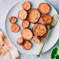 roasted sweet potato rounds on a white plate with a gold fork