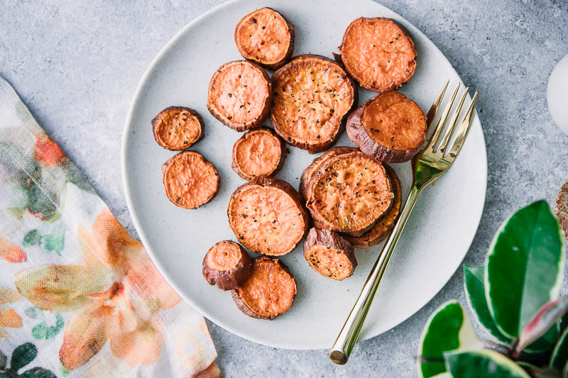 roasted sweet potato rounds on a white plate with a gold fork