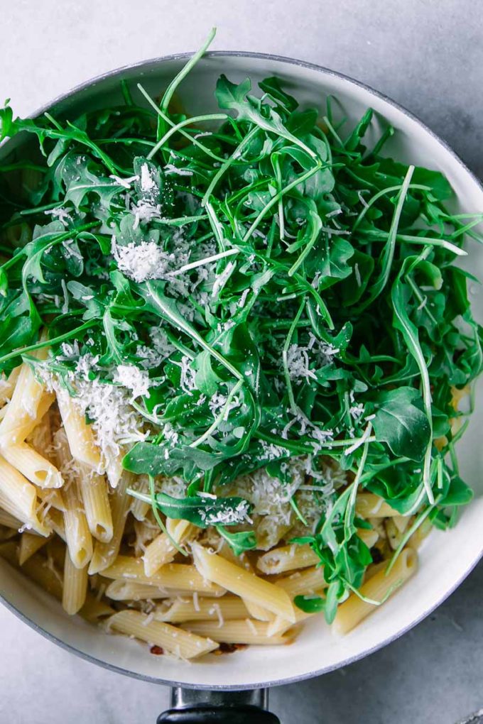 fresh arugula leaves in a pan with penne pasta