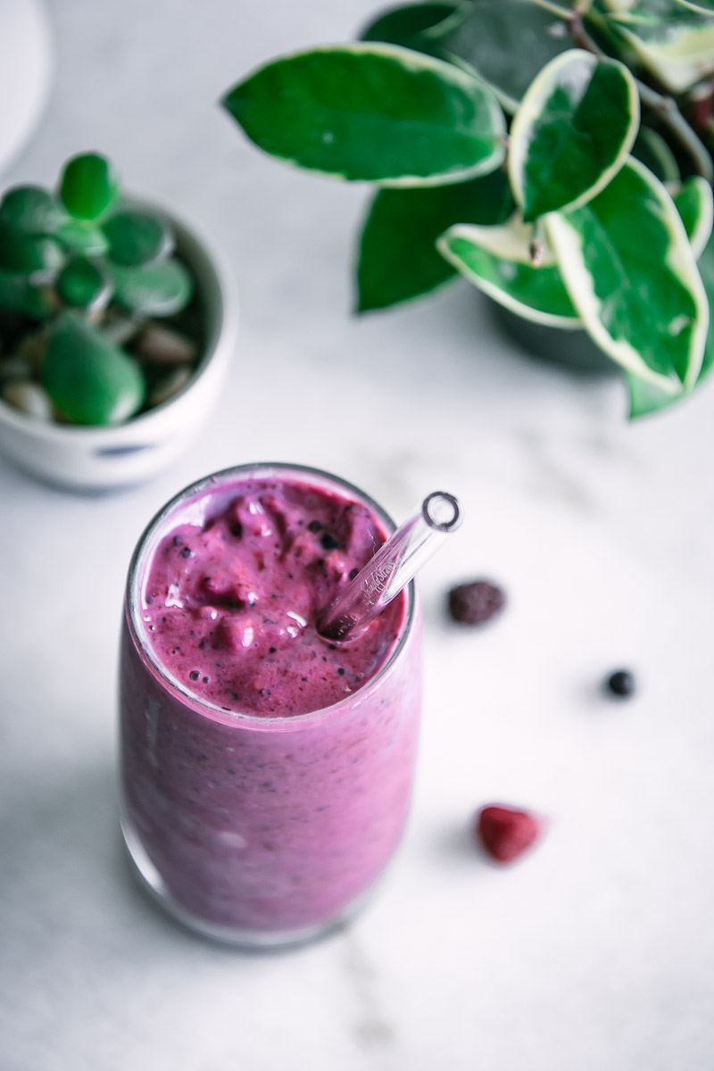 a purple smoothie with blueberries, raspberries, and blackberries on a white breakfast table