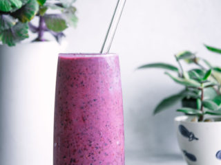 a purple smoothie in a tall glass with a glass straw with the words "triple berry banana smoothie" in black cursive writing