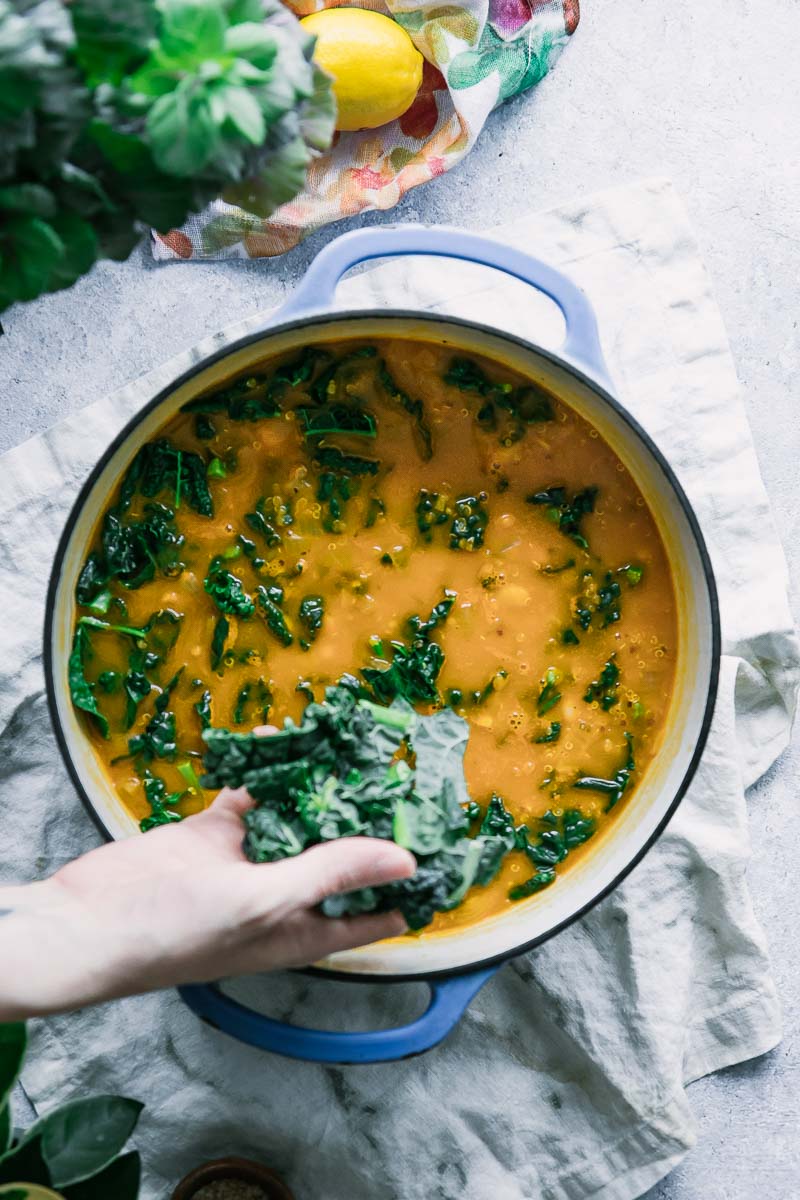 a hand adding kale to a soup pot filled with white bean kale quinoa soup