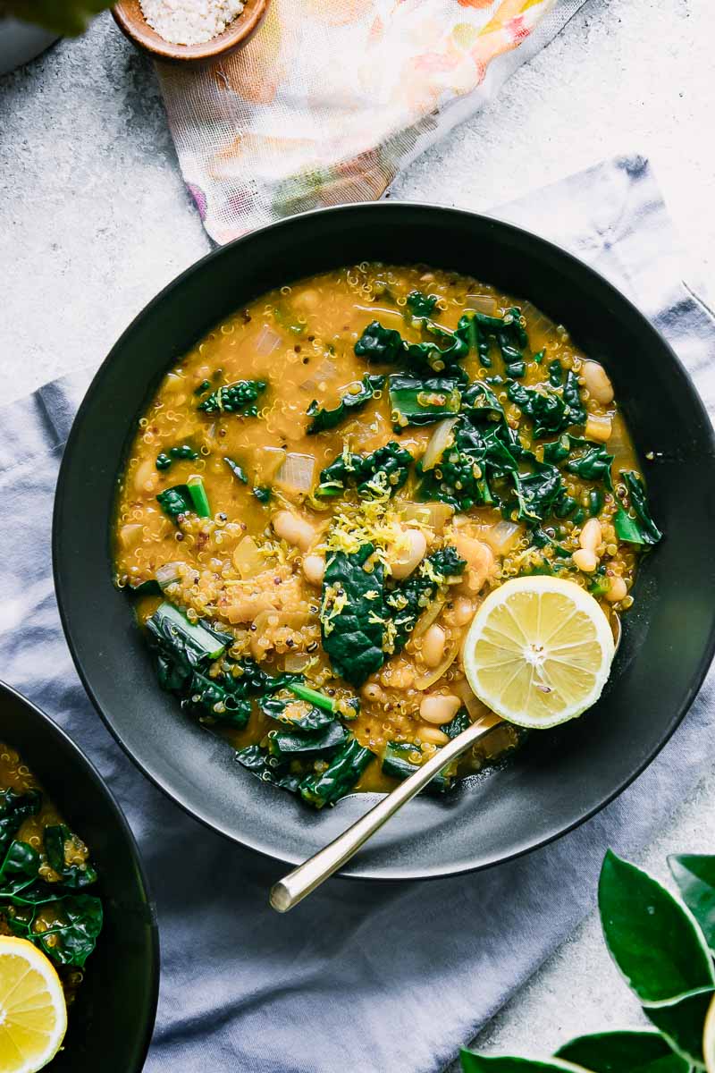 a black bowl with white chili with kale and a lemon slice on a blue table with flowers