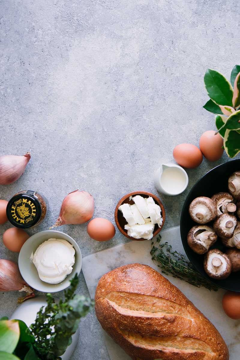 bread, eggs, mushrooms, goat cheese, cream, shallots, and mustard on a blue table