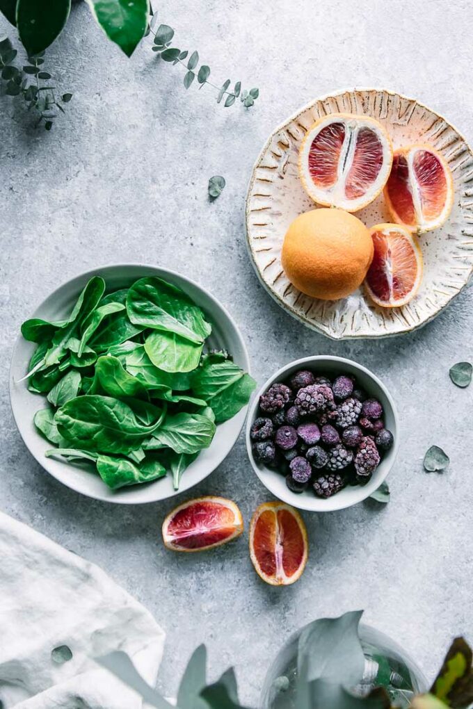 bowls of spinach, raspberries, and orange slices on a blue table