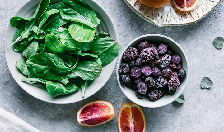 a bowl of spinach, berries, and oranges on a white table