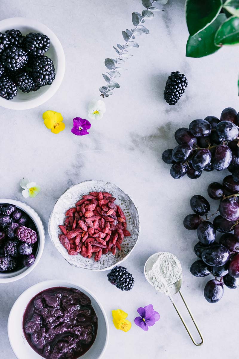 bowls of purple foods like blackberries, grapes, goji berries, and acai in small bowls on a white table