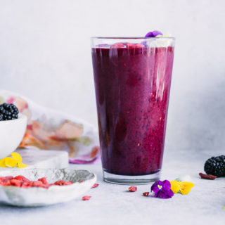 a purple smoothie on a white counter with a bowl of goji berries