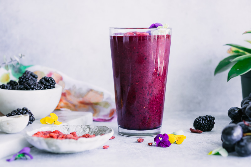 a berry smoothie on a white counter with a bowl of goji berries