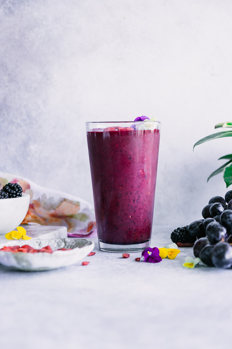 a purple smoothie on a white table and a blue background with a bowl of berries