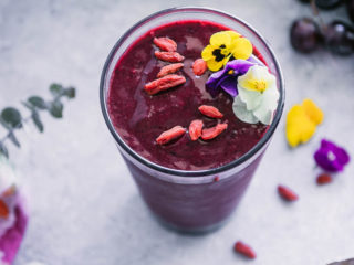 acai smoothie in a glass with flowers, berries, and grapes