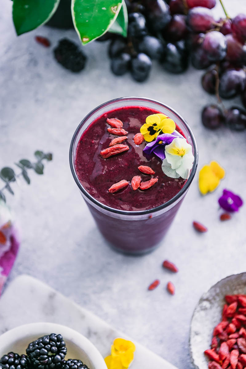 acai smoothie in a glass with flowers, berries, and grapes
