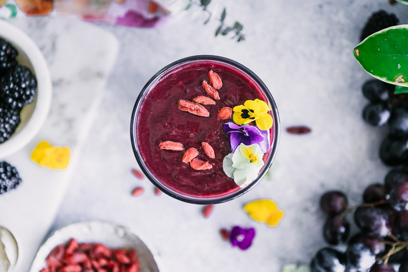 the top of a purple smoothie with goji berries and colorful edible flowers