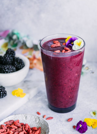 a purple smoothie in a glass with edible flowers on a white table