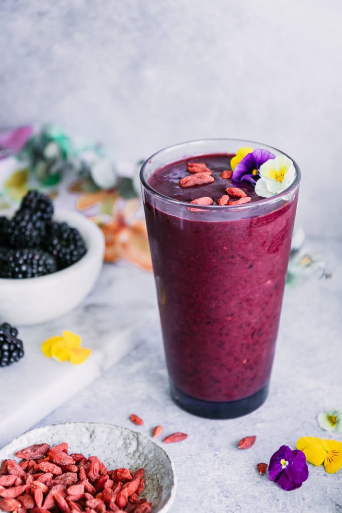 a purple smoothie in a glass with edible flowers on a white table