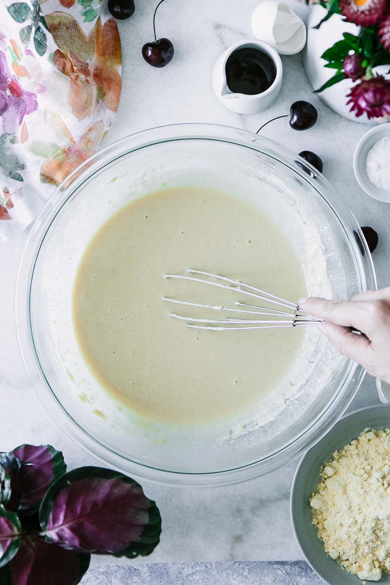 a hand mixing pancake batter on a blue table with cherries and flowers