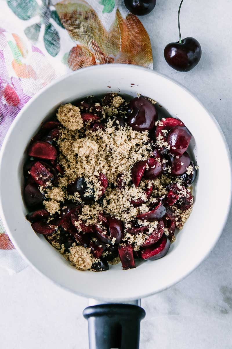 a closeup of cherries and brown sugar in a white saucepan