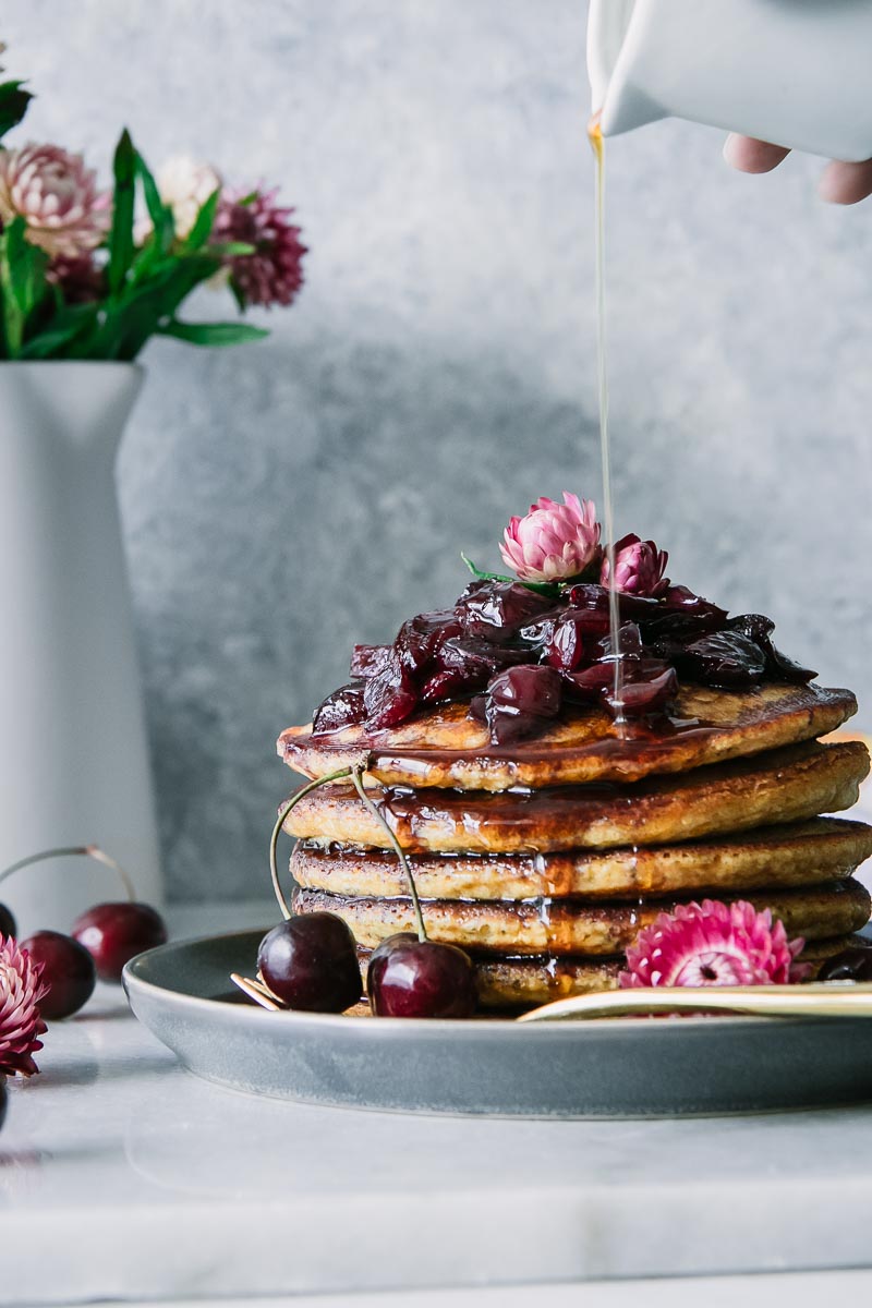 a stack of cornmeal pancakes, or hoecakes, with cherry sauce and a drizzle of maple syrup