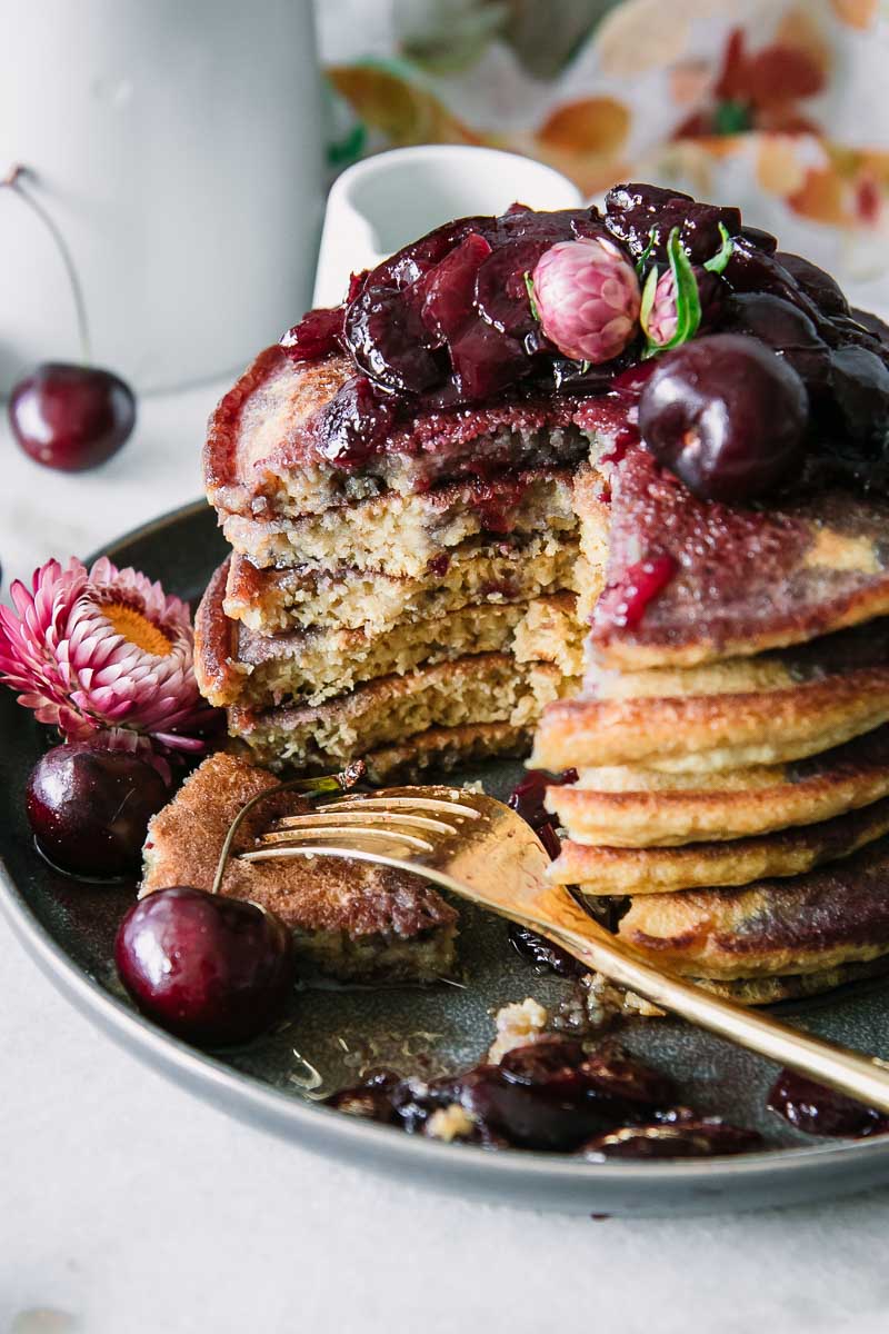 a stack of pancakes with cherries and a gold fork on a blue plate