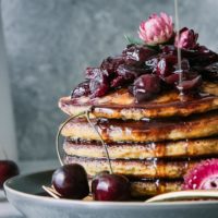 a stack of pancakes with cherries and maple syrup drizzling