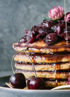 a stack of pancakes with cherries and maple syrup drizzling