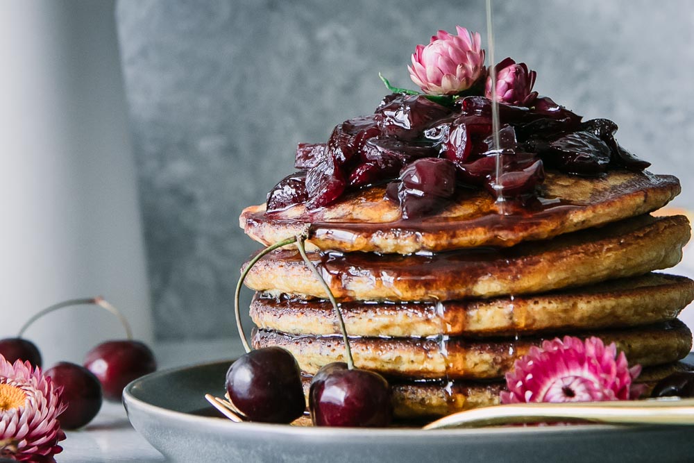 a stack of pancakes with cherries and maple syrup drizzling
